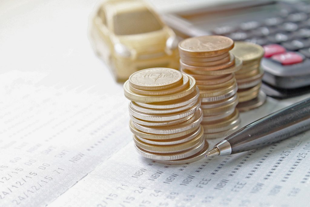 Miniature car model, coins stack, calculator and saving account book or financial statement on office desk table